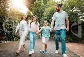 Happy young caucasian family of four holding hands and going for a walk in the neighbourhood. Carefree parents with their two children leaving their residence and going for a sunny stroll surrounded by greenery