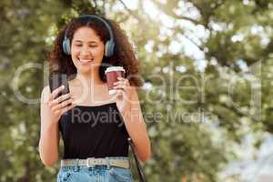 Beautiful young mixed race woman listening to music and texting on her phone outside. Confident and happy african american female walking outdoors during the day with a fresh takeaway coffee in hand
