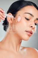 One beautiful mixed race woman using a rose quartz derma roller during a selfcare grooming routine. Young hispanic woman using anti ageing tool against grey copyspace background