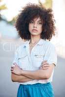 A young female mixed race woman standing with her arms crossed outside looking cool and confident with great style. Hispanic hipster woman with a curly afro in a cool outfit against a urban background