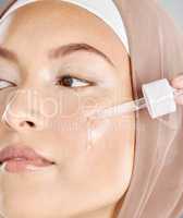 A young woman applying antiaging facial serum to her face and skin. Beautiful muslim girl wearing a hijab trying retinol with a dropper as her skincare routine and beauty treatment regime