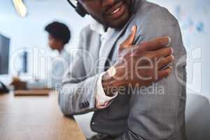 Closeup of one stressed african american businessman suffering with arm and shoulder pain in an office. Entrepreneur rubbing muscles and body while feeling tense strain, discomfort and hurt from bad sitting posture and long working hours at desk