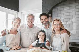 . Happy smiling caucasian family baking together in the kitchen. Little cheerful girl helping her parents and grandparents bake. Senior woman and man cooking with their family.