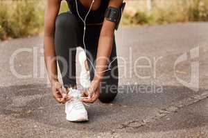 One african american female athlete tying her laces before starting her outdoor workout. A dedicated black woman listening to music and preparing for a run outside. Health and fitness is her lifestyle