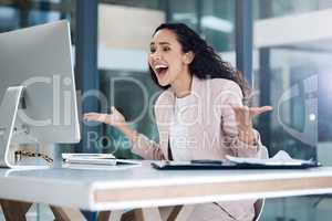 Young happy mixed race businesswoman looking shocked and amazed using a desktop computer in an office. One cheerful hispanic businessperson smiling making a hand gesture while looking at a pc screen at work