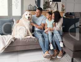 A happy mixed race family of three relaxing on the sofa with their dog. Loving black family being affectionate with a foster animal. Young couple bonding with their daughter and rescued puppy at home