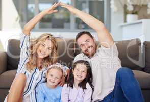 Smiling couple with little kids sitting and making symbolic roof with hands over children. Cheerful family sitting together on floor in new house on relocation day. Covered and protected by insurance