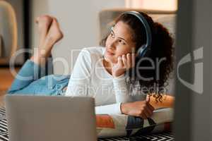 woman dreaming and listening to music. Young woman listening to music through headphones on her laptop. Girl lying on the floor thinking. Young woman enjoying her music on a computer at home
