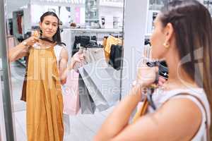 Beautiful young woman looking at clothing in a mirror in a department store. Trying on clothes while shopping for fashion sales. Retail therapy is just what she needed. The customer is always right