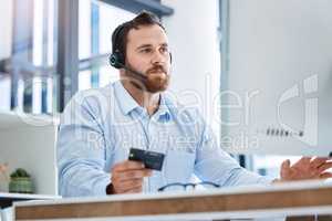 Waiting for payment confirmation. Shot of a young call centre agent using a credit card while working on a computer in an office.