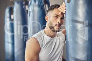 Portrait of tired boxer leaning on punching bag. Exhausted mma fighter resting after workout in the gym. Bodybuilder boxing routine in the gym. Strong fit man tired after combat training