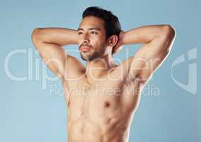 Handsome young hispanic man standing shirtless in studio isolated against a blue background. Mixed race topless male athlete looking confident, healthy and fit. Exercising to increase his strength