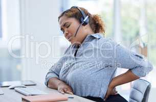 One young stressed mixed race female call centre telemarketing agent suffering with lower back pain in an office. American american businesswoman feeling tense strain, discomfort and hurt to spine with poor sitting posture and long working hours at desk