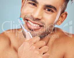 Portrait of one smiling young indian man brushing his teeth against a blue studio background. Handsome guy grooming and cleaning his mouth for better oral and dental hygiene. Brush twice daily to prevent tooth decay and gum disease