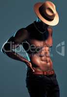 Fashionable african American model posing shirtless against blue studio background with copyspace. Sexy, unknown black man with attitude showing bare six pack while wearing hat. Masculine and muscle