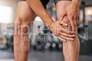 Closeup of one caucasian man holding his sore knee while exercising in a gym. Male athlete suffering with painful leg injury from fractured joint and inflamed muscles during workout. Struggling with stiff body cramps causing discomfort and strain