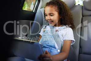 Entertainment secured. Cropped shot of an adorable little girl using her tablet while sitting in the backseat of a car.