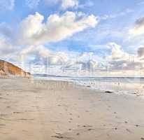 The beach of Torrey Pines, San Diego, California. Landscape of empty beach showing shoreline. Walkers footprints remain in the sand as the sun starts setting and the clouds come over the sky.