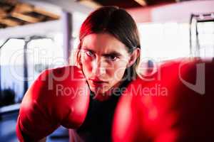 Portrait of one fit young caucasian man wearing boxing gloves with neon red light reflecting on face while training in a gym. Strong focused boxer practising for competition fight. Fierce guy ready to strike with a hit and jab while learning self defence