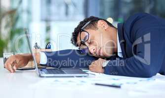 One exhausted mixed race businessman wearing glasses while sleeping at his desk in an office. Young entrepreneur feeling overworked, tired and demotivated. Lazy man slacking and ignoring deadlines by taking a nap. Burnout and stress in the workplace