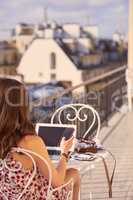 Follow me for amazing Parisian sights to see. Shot of a woman using a smartphone and laptop while having breakfast on the balcony of an apartment overlooking Paris, France.