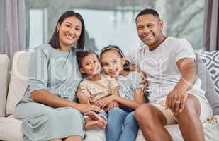 Happy and affectionate young mixed race family of four sitting on a sofa in the living room at home. Married couple sitting with their son and daughter in the lounge. Mom, dad, bother and sister