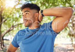 Fit athletic man smiling while stretching his arms during a workout at the park. Hispanic man doing warm-up exercises outdoors on a sunny day. Athletic man taking a break from a fitness routine