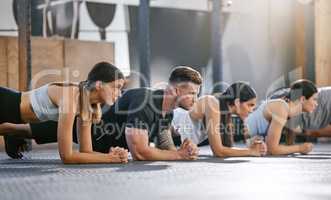 Diverse group of fit people doing bodyweight plank hold exercises together in a gym. Focused athletes training to build muscle, enhance upper body, strengthen core and increase endurance for workout in a fitness class