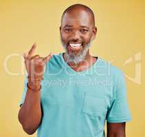 Happy mature african man expressing a rock and roll symbol gesture with his hands against a yellow studio background. Carefree, cool and confident black man making horn gesture to show good vibes