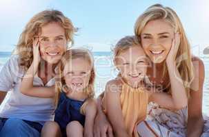 Portrait of a carefree family relaxing and bonding on the beach. Two cheerful little girls having fun with their mother and grandmother on holiday. Mom and grandma love their cute little girls