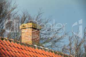Red brick chimney designed on asbestos slate roof of house building outside with a sky background. Exterior construction architecture of escape chute built on rooftop for fireplace smoke and heat