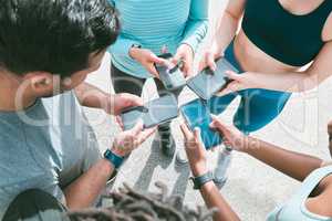 Closeup of diverse group of sporty people from above using cellphones with blank screens in synchronicity while standing in a circle around each other. Hands of athletes browsing online and searching the internet in a huddle. Downloading and sharing media