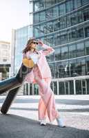 One fashionable young mixed race woman wearing stylish sunglasses and a trendy pink suit while posing in the city. One female only looking carefree, cool and confident while exploring town outside