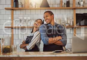 Cheerful businesspeople standing in their cafe kitchen. Business partners standing back to back in their coffeeshop. Two entrepreneurs arms crossed in their restaurant kitchen.