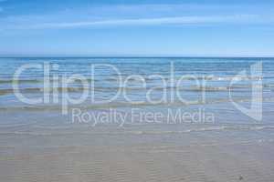 Small ocean waves on the shore against a clear blue sky with copy space. Landscape of the wide open sea or beach with calm water on a bright sunny day. Sea surface with ripples on the horizon