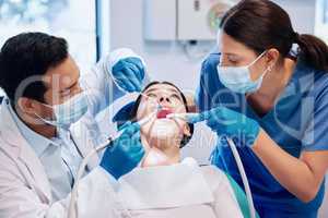 Theyre hard at work. Shot of a young dentist working on a patients teeth with his assistant.