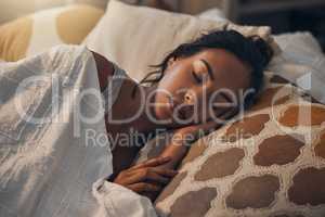 A beautiful young mixed race woman sleeping in a soft comfortable bed at home. One hispanic female feeling exhausted and resting in a comforting bed