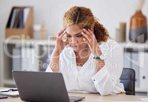 Young mixed race businesswoman suffering from a headache while working on a laptop in an office at work. One stressed hispanic businessperson suffering from anxiety and looking upset