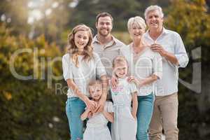 Portrait of a smiling multi generation caucasian family standing close together in the garden at home. Happy adorable girls bonding with their mother, father, grandfather and grandmother in a backyard
