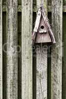 Old, wooden, and rustic bird feeder hanging on a fence in a backyard garden. Closeup of a vintage birdhouse on a wall outside. Built enclosures for birds in their natural environment and habitat