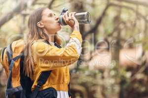Fit caucasian woman taking a break to drink some water while wearing a backpack and out for a hike in nature on a sunny day