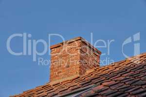 Copy space with a chimney on the rooftop of a house or building against a blue sky background. Brick construction of an exterior escape chute for ventilation of air and smoke from a fireplace or oven