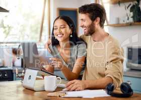 Happy young interracial couple calculating their budget using wireless devices at home. Smiling young caucasian man working on laptop while hispanic wife browses social media on digital tablet