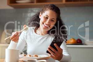 Woman eating sushi and using her cellphone. Young woman sending a text on her smartphone while eating seafood. Happy woman enjoying a meal at home. Young girl eating savoury fish