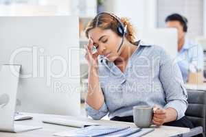 Stressed call center agent with a headache. Businesswoman working in customer service looking upset. IT support assistant suffering with a migraine. Frustrated businesswoman drinking coffee
