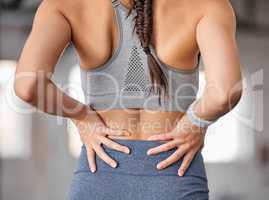 Closeup of one caucasian woman holding her sore lower back while exercising in a gym. Female athlete suffering with painful spine injury from fractured joint and inflamed muscles during workout. Struggling with stiff body cramps causing discomfort