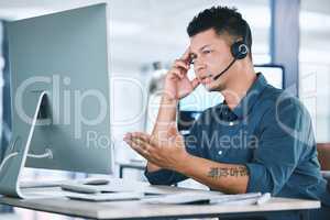 One stressed and confused hispanic call centre agent talking on headset while working on broken computer in an office. Anxious male consultant having problems with slow internet connection failure error while panic with crisis and difficult customers