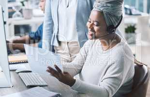 African american call centre telemarketing agent reading paperwork while receiving training and assistance from supervisor in an office. Confident female consultant troubleshooting solution with manager. Colleagues operating helpdesk together