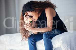 Grief is love not wanting to let go. a young woman looking sad while holding a teddy bear in a bedroom at home.