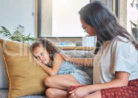 Sad depressed little girl lying on the couch and looking away while worried mother psychologist tries to talk to her. Loving caring mother trying to communicate with upset daughter. Young hispanic mother asking little girl whats wrong while trying to comf